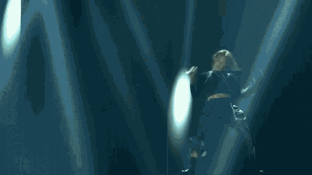 a woman in a black top and black pants is dancing in front of a blue bag .