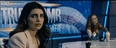 two women are sitting at a table in front of a sign that says tru mb
