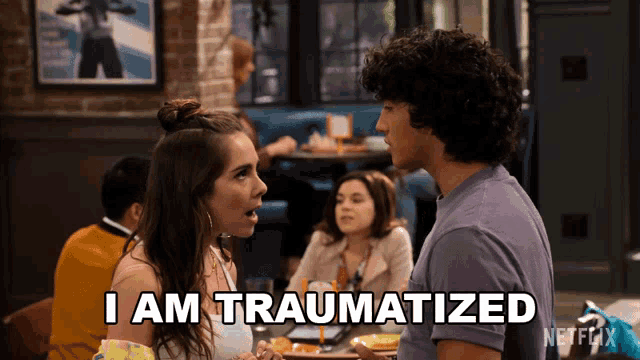a man and a woman are sitting at a table and the woman is saying i am traumatized