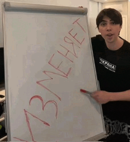 a man is standing in front of a whiteboard with russian writing on it and pointing at it .
