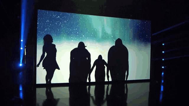a silhouette of a family standing in front of a large screen