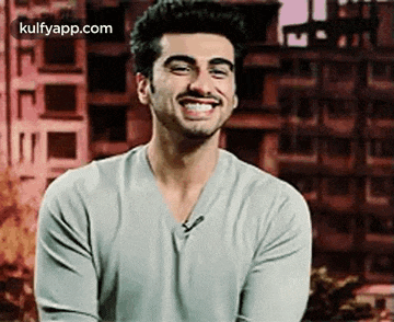 a man is smiling and looking at the camera while wearing a grey shirt .