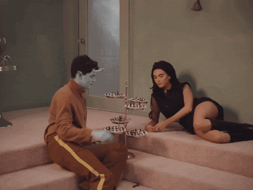 a man with blue paint on his face sits next to a woman kneeling on stairs