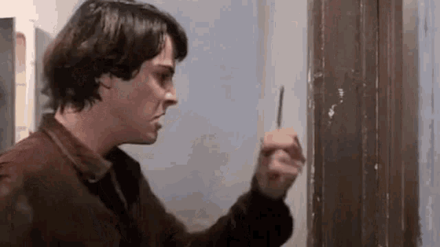 a man is holding a screwdriver in his hand while standing next to a door .