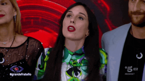 a woman stands in front of a screen that says grandefratello on it