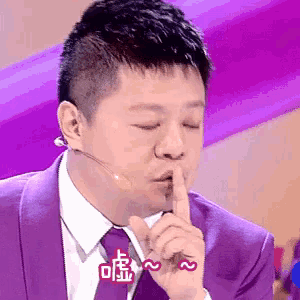 a man wearing a purple suit and tie is holding his finger to his lips .