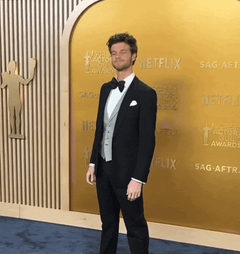 a man in a tuxedo stands in front of a wall that says netflix on it