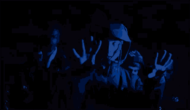 a man in a hooded jacket is holding a piece of paper in his hands in a dark room .