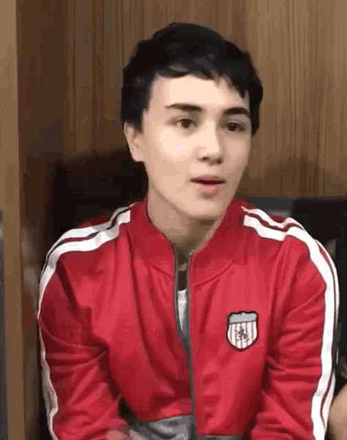 a young man wearing a red jacket with white stripes on the sleeves is sitting down .