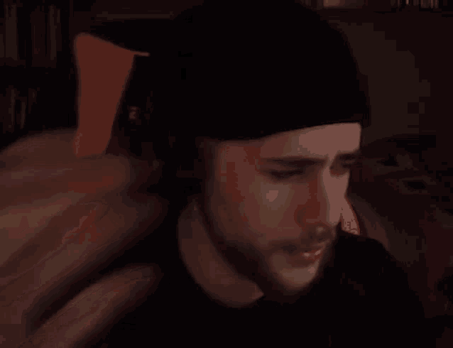 a man with a beard wearing headphones and a beanie is sitting in a chair in a dark room .