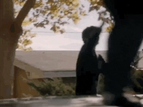 a person is standing on a sidewalk next to a tree holding a gun .