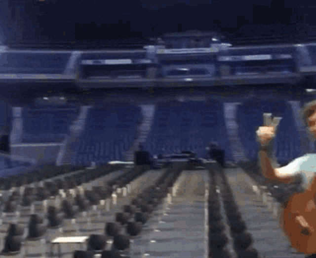 a man is holding a guitar in an empty stadium