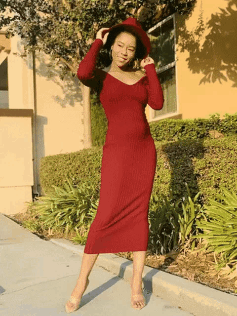 a woman wearing a red dress and a red hat is standing on a sidewalk