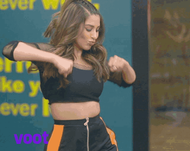 a woman in a black crop top is dancing in front of a sign that says voot