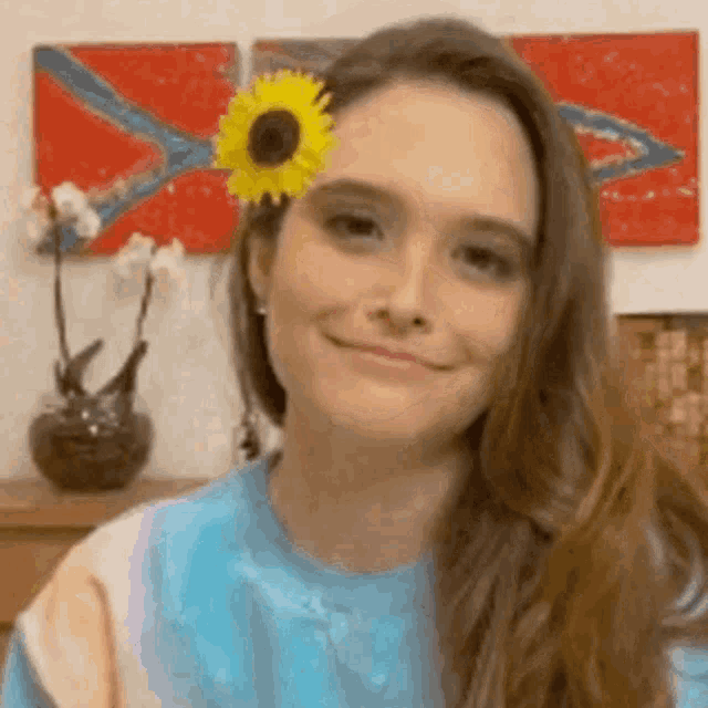 a woman wearing a blue shirt and a sunflower in her hair is smiling .