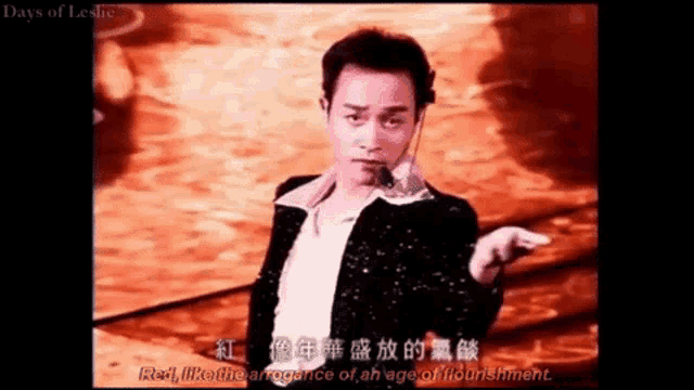 a man in a black jacket is standing in front of a red background with chinese writing on it .