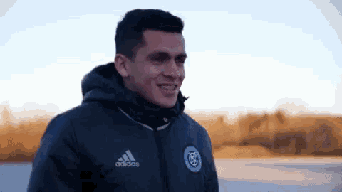 a man wearing an adidas jacket is smiling while standing in the snow .