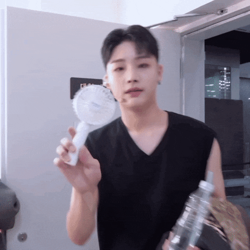 a man in a black shirt is holding a fan and a water bottle