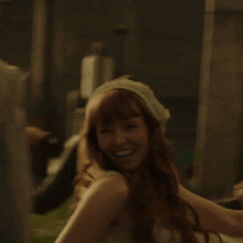 a woman with long red hair wearing a white head scarf smiles