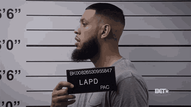 a man with a beard is holding a lapd pac mugshot