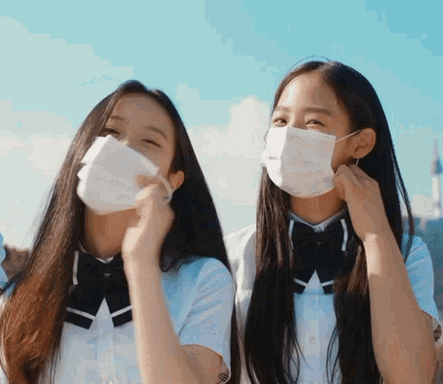 two girls wearing white face masks with a blue sky in the background
