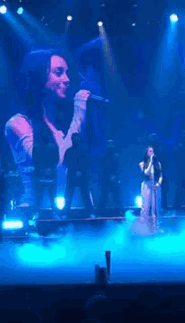 a woman is singing into a microphone on a stage in front of a large screen