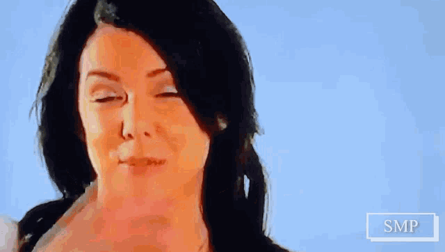 a close up of a woman covering her mouth with her hand with a blue sky in the background