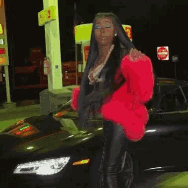 a woman in a red fur coat is standing next to a black car