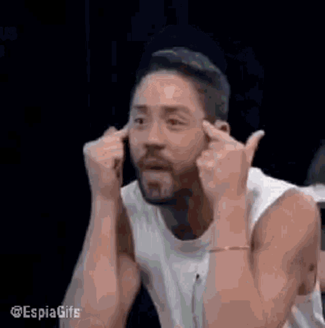 a man with a beard is holding his hands to his ears and making a funny face .