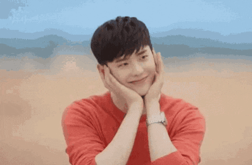 a young man in a red shirt is holding his face with his hands .