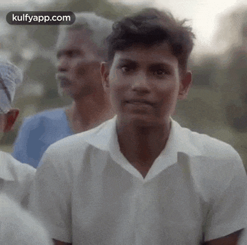 a young man in a white shirt is looking at the camera while standing in a crowd of people .