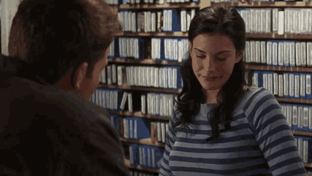 a man and a woman are standing in front of a bookshelf filled with blue binders ..