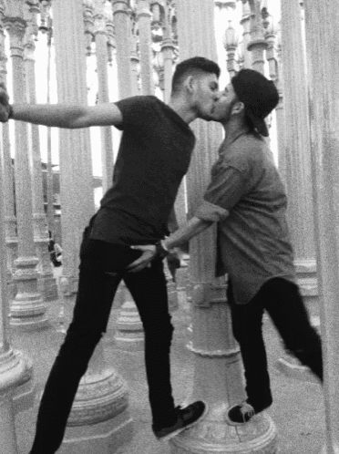 a couple of men kissing in front of columns