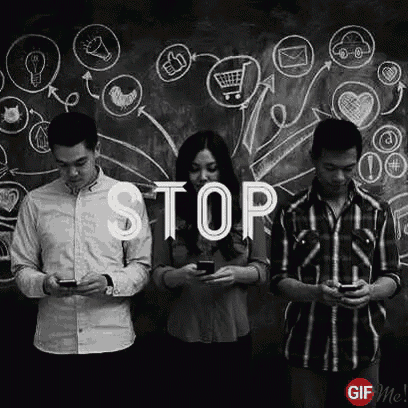 a group of people standing next to each other looking at their phones in front of a chalkboard .