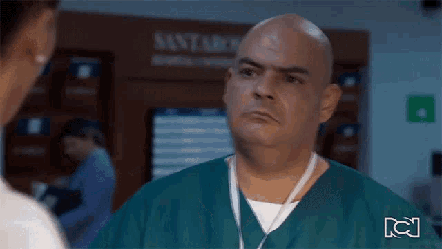 a bald man in a green scrub is talking to a woman in a hospital