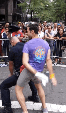 a man in a purple shirt is being held by a police officer while a crowd watches