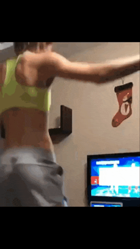 a woman is dancing in front of a television with a christmas stocking hanging from the wall .