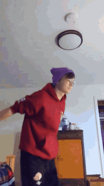 a person wearing a red hoodie and a purple hat is dancing