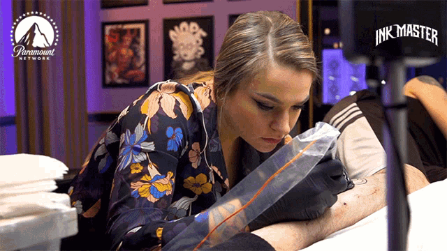 a woman is getting a tattoo on a man 's arm in a paramount network advertisement