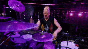 a man with a mohawk is playing drums in a dark room with purple lights