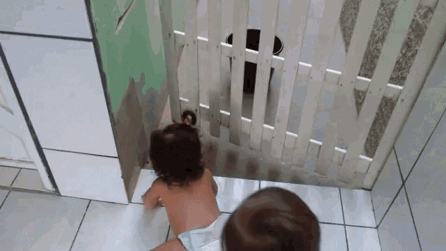 a baby in a diaper is looking through a wooden gate