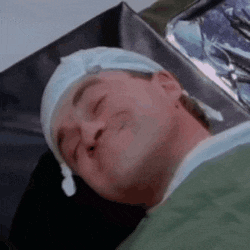 a man laying in a hospital bed with his eyes closed and a hat on his head