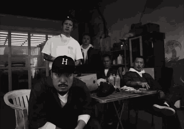 a man wearing a baseball cap with the letter h on it sits next to two other men