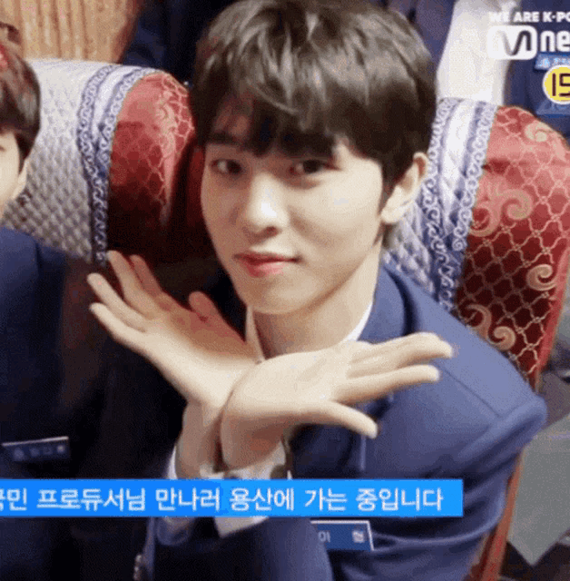 a young man in a blue suit is sitting in a chair with a sign that says we are k-pop mnet