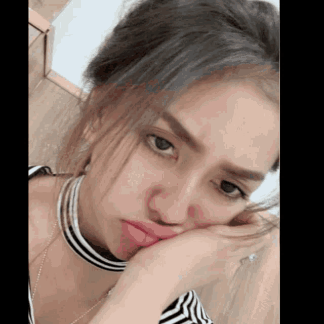 a woman wearing a striped shirt and a choker holds her hand to her face