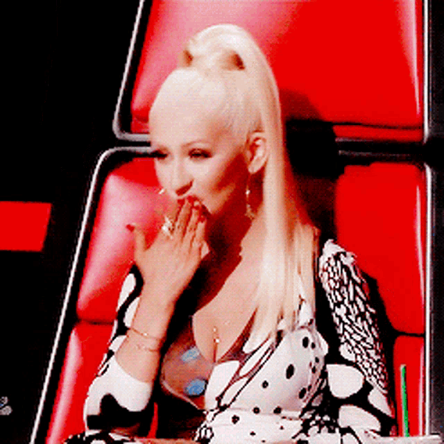 a woman is sitting in a red chair with her hand on her mouth