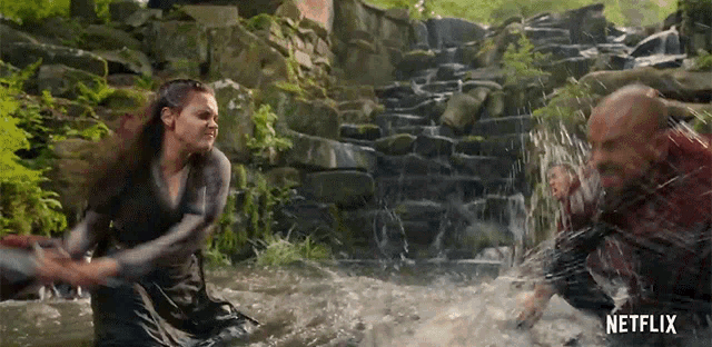 a man and a woman are fighting in a waterfall with a netflix logo in the background .