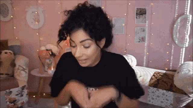 a woman with curly hair is wearing a black t-shirt and making a funny face .