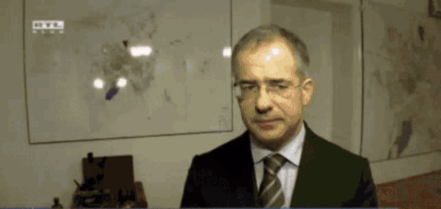 a man in a suit and tie is standing in front of a wall with a map of the world on it
