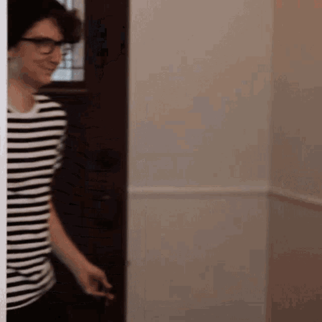 a man wearing glasses and a striped shirt is standing next to a door .